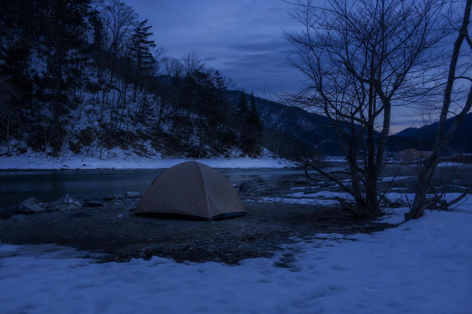 冬の夕方のキャンプ場。雪の残る地面に張られたドーム型テントの外観を少し離れて写す。テントの中にも周りにもストーブ・焚き火・炎は写さない