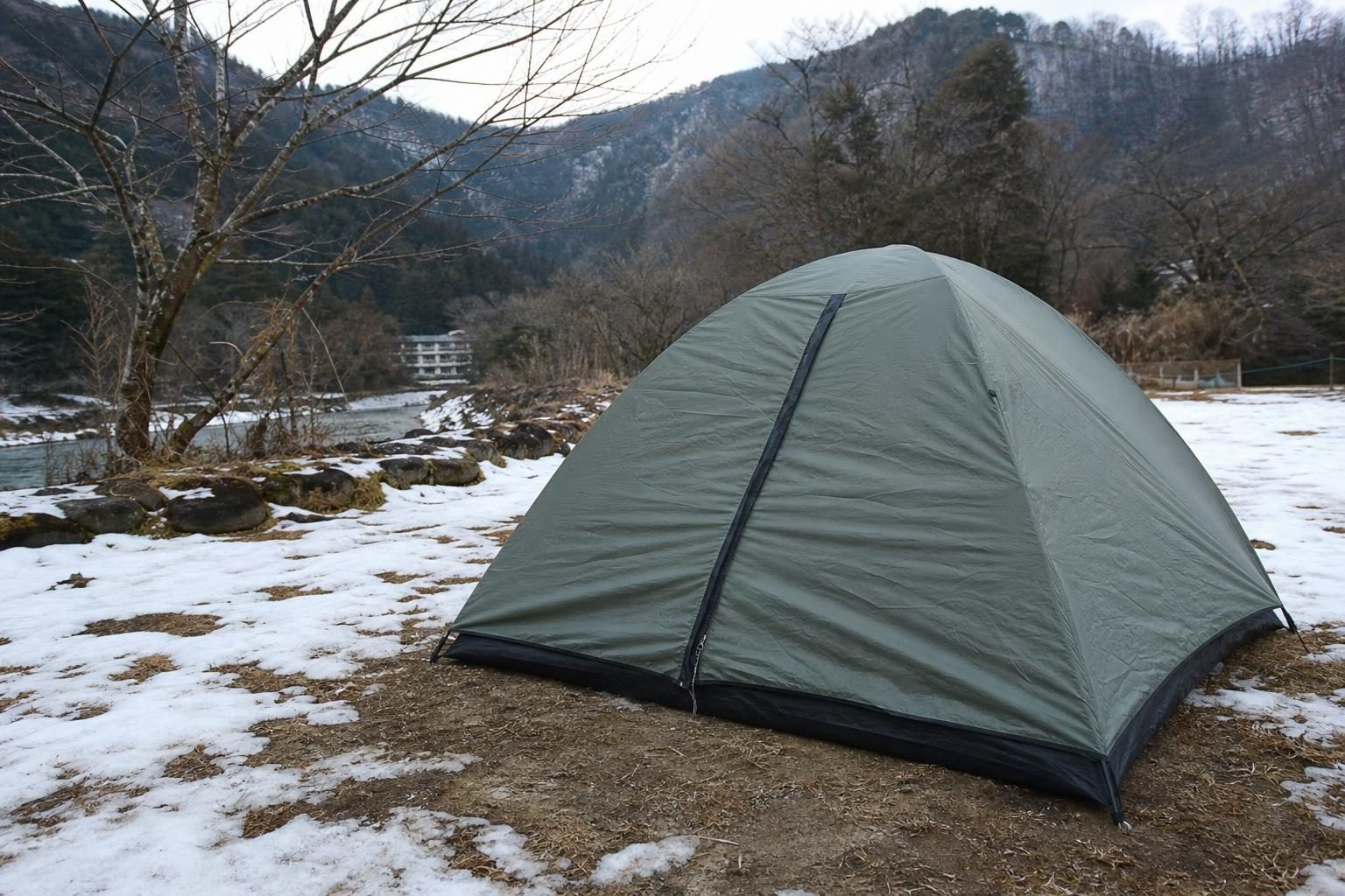 冬の昼、雪の残るキャンプ場に張られた、入口を閉じた緑のドーム型テント